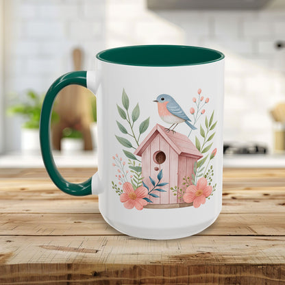 White ceramic mug with green handle and interior, featuring a watercolor pink birdhouse and bluebird design.