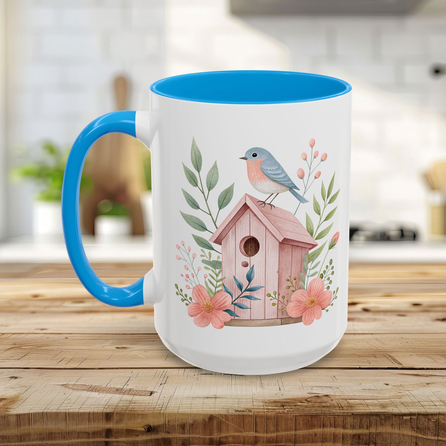 White ceramic mug with blue handle/interior, featuring a watercolor pink birdhouse, bluebird, and peach blossoms.