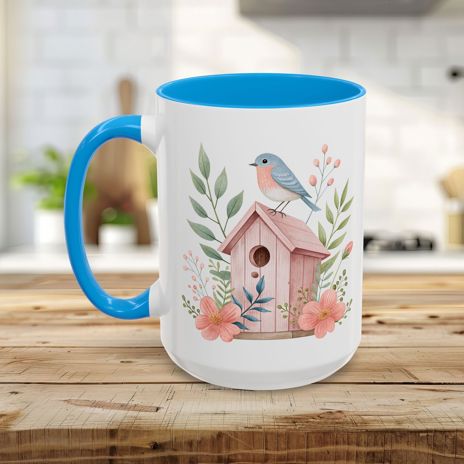 White ceramic mug with blue handle/interior, featuring a watercolor pink birdhouse, bluebird, and peach blossoms.