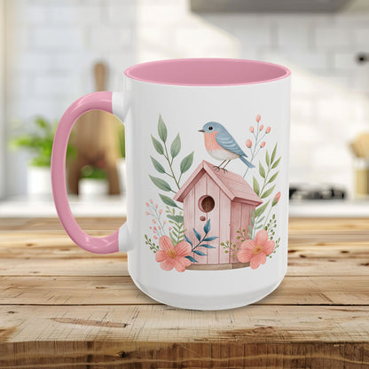 White ceramic mug with pink interior/handle, featuring a watercolor bluebird on a pink birdhouse with peach blossoms.