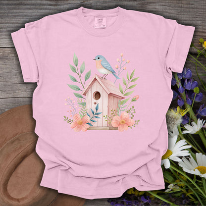 Pink garment-dyed cotton t-shirt with a watercolor birdhouse, blue bird, and floral design.
