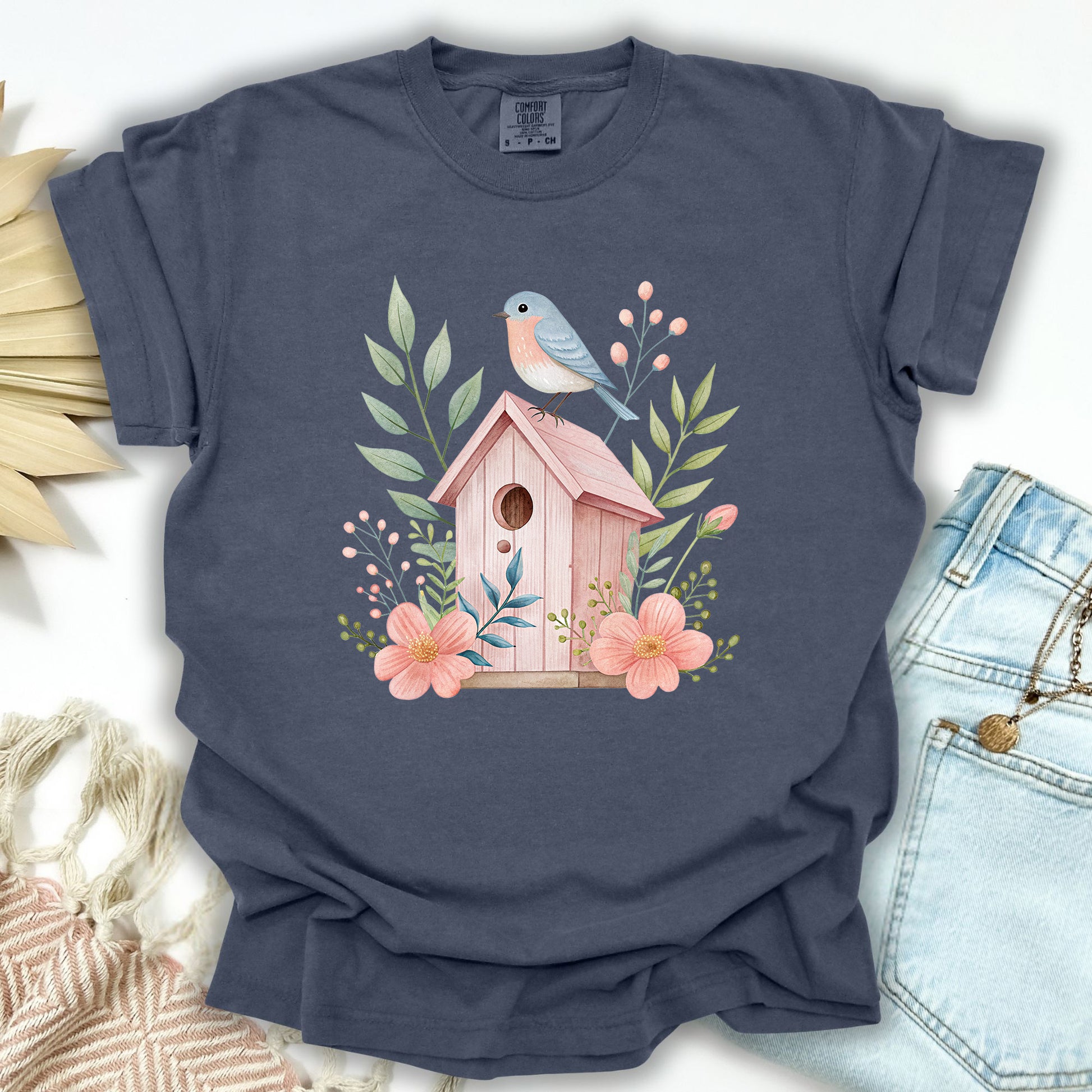 Denim S garment-dyed t-shirt with a watercolor pink birdhouse, blue bird, and floral design.