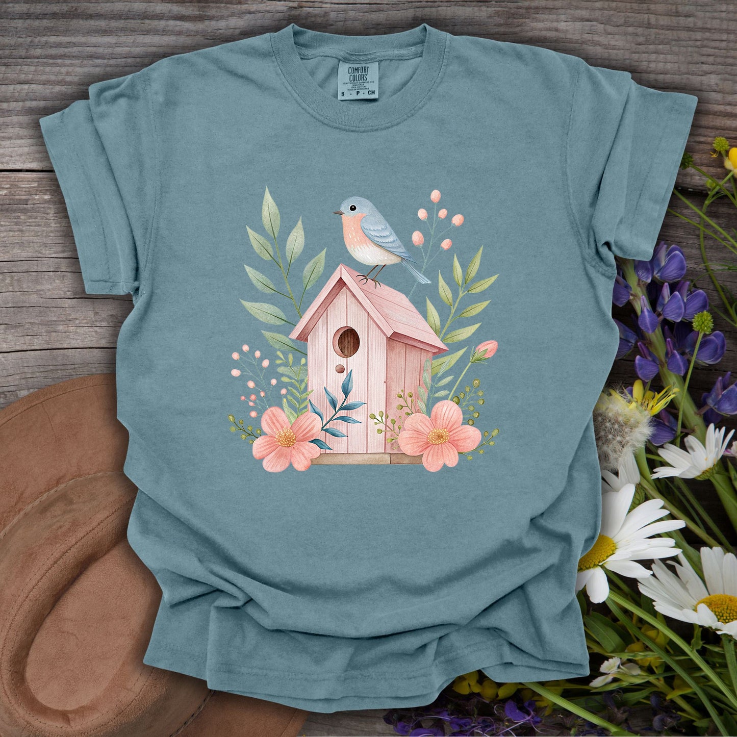Ice Blue S-size garment-dyed cotton t-shirt with a watercolor pink birdhouse, blue bird, and floral design.