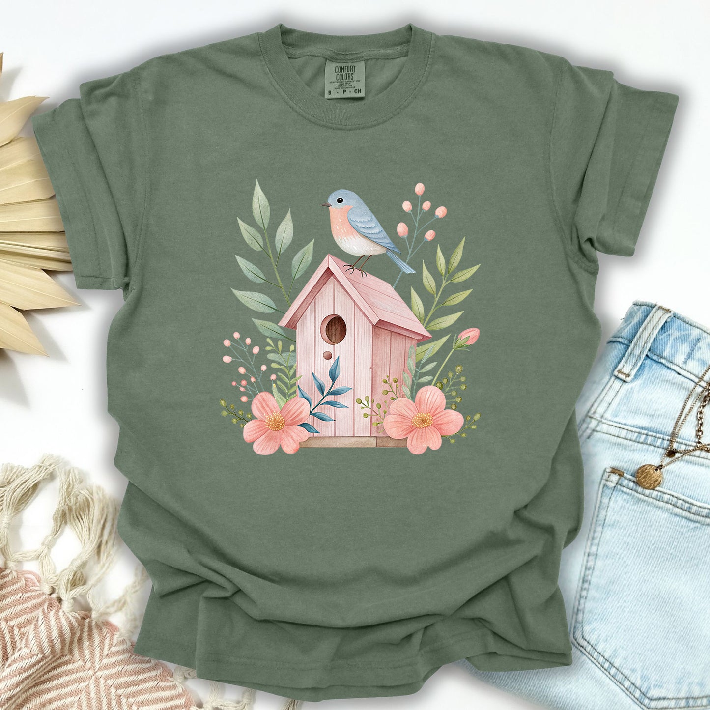 Moss green, relaxed-fit cotton t-shirt with a watercolor pink birdhouse, blue bird, and floral design.
