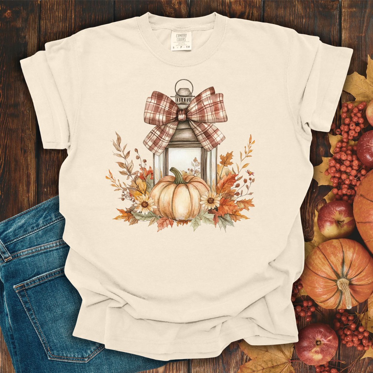 Ivory garment-dyed tee with a rustic autumn lantern, pumpkin, sunflowers, and plaid bow design.