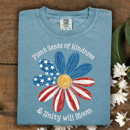 Ice Blue Comfort Colors t-shirt with "Plant Seeds of Kindness & Unity will Bloom" text and a daisy with an American flag design.