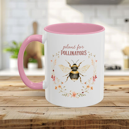 White ceramic mug with pink handle and interior, featuring a watercolor bee and "plant for pollinators" text.
