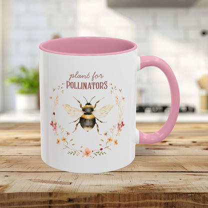 White ceramic 11oz mug with pink handle and interior, featuring a watercolor bee and "plant for pollinators" text.