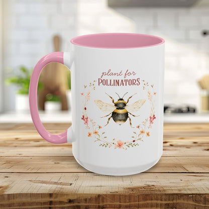 White ceramic mug with pink handle and interior, featuring a watercolor bee and "plant for pollinators" text.