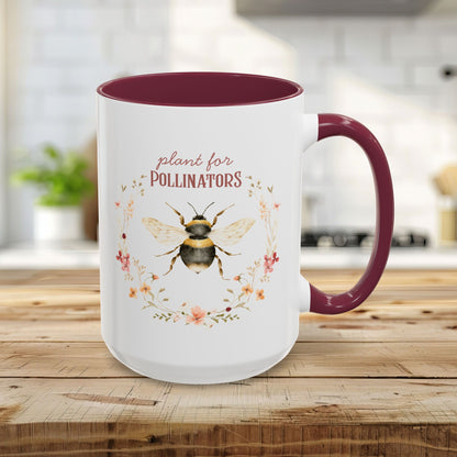 15oz white ceramic mug with maroon interior and handle, featuring a watercolor bee and "plant for pollinators" text.
