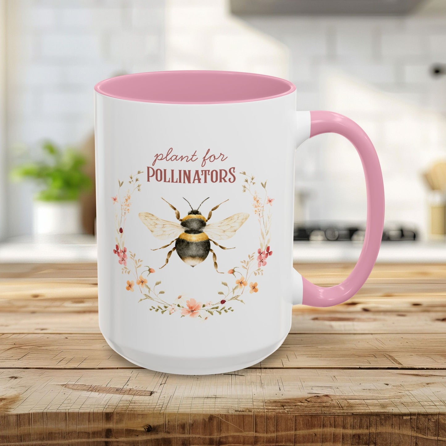 White 15oz ceramic mug with pink handle and interior, featuring a watercolor bee and "plant for pollinators" text.