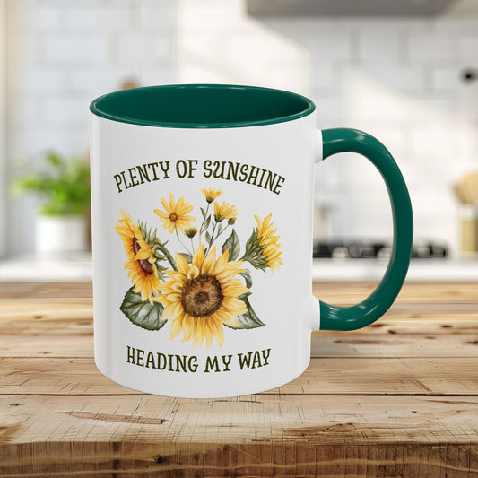 White ceramic 11oz mug with green interior and handle, featuring watercolor sunflowers and "Plenty of sunshine heading my way" text.
