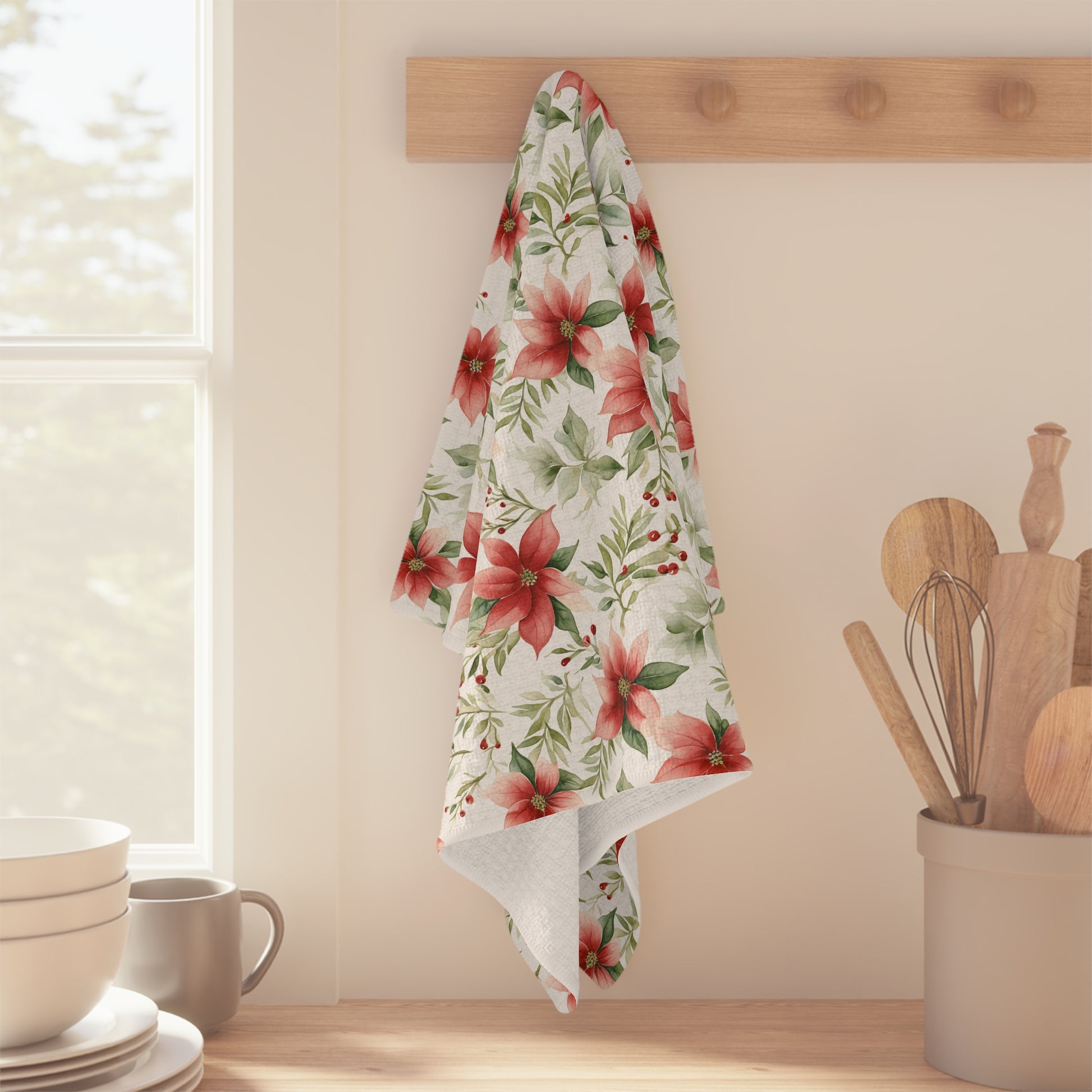 Watercolor poinsettia microfiber tea towel with red and green floral design hanging on a wooden peg rack.