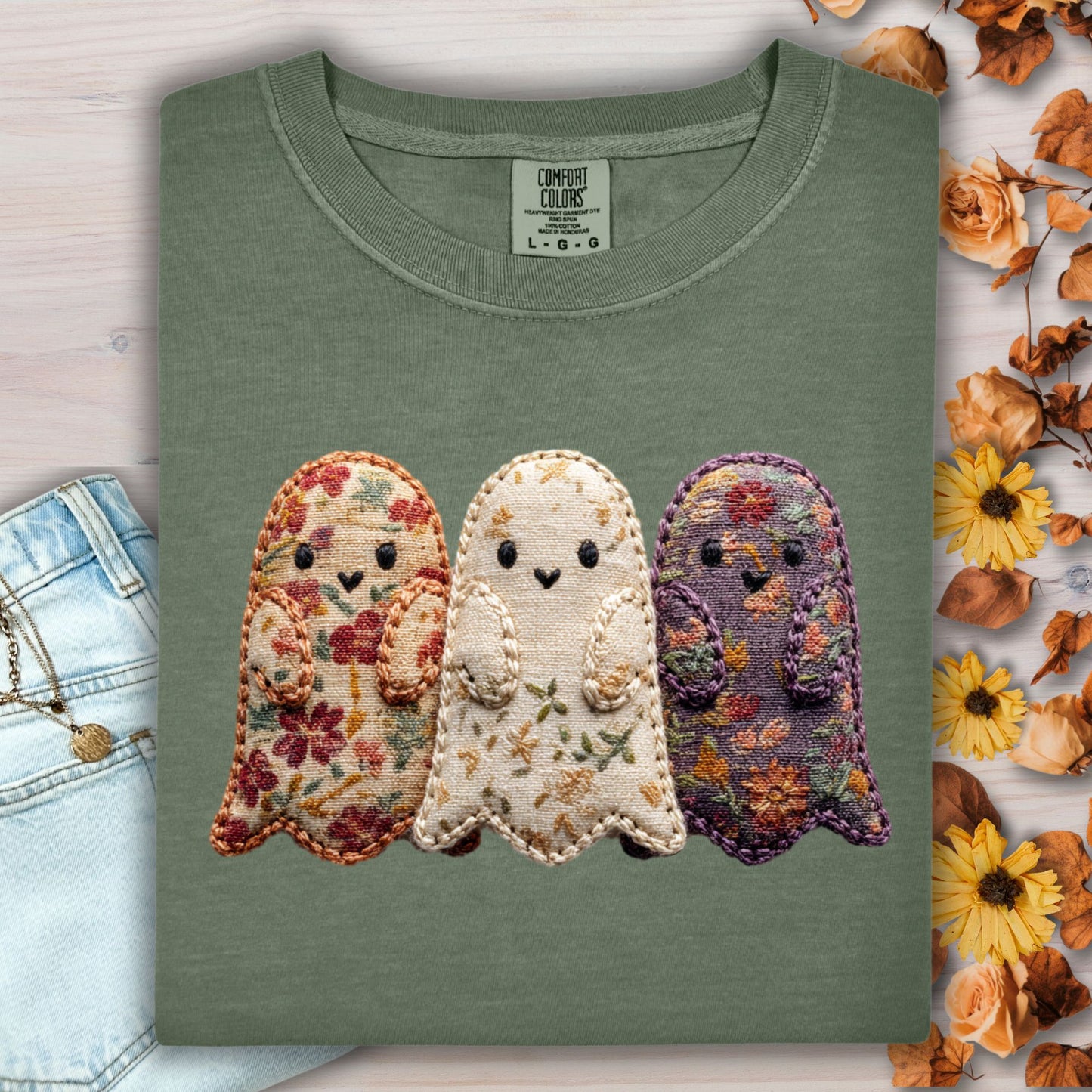 Moss green Comfort Colors t-shirt with three embroidered floral fabric ghosts, light wash jeans, and fall leaves.