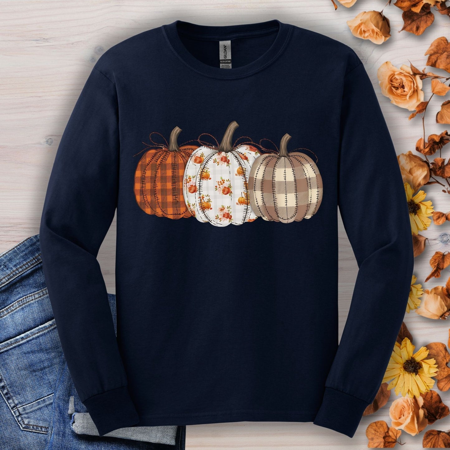 Navy long sleeve tee with 3 cottagecore quilted pumpkins, surrounded by fall leaves and jeans.