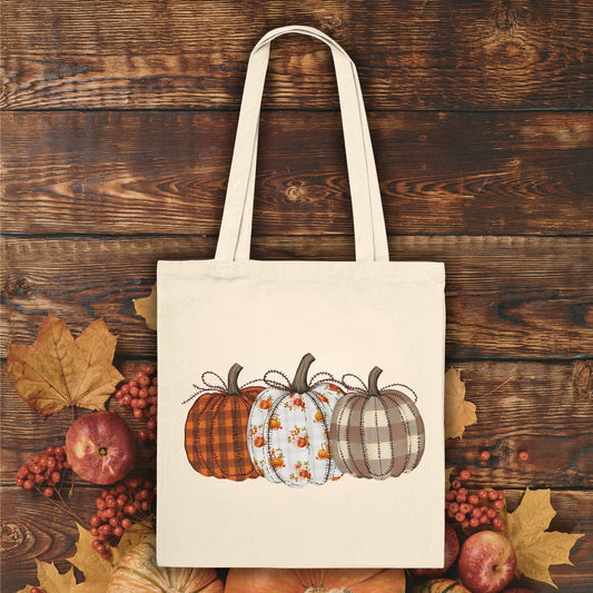 Natural cotton tote bag with a "Quilted Pumpkins" design, featuring three patterned pumpkins.