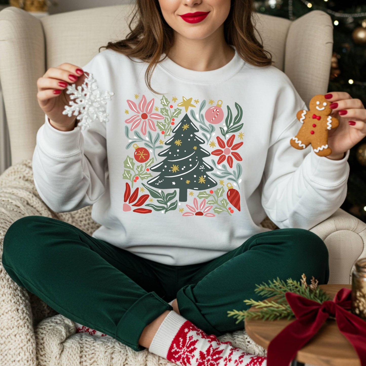 White Gildan fleece sweatshirt with a colorful retro Christmas tree and floral design, worn by a person holding a snowflake and gingerbread man.