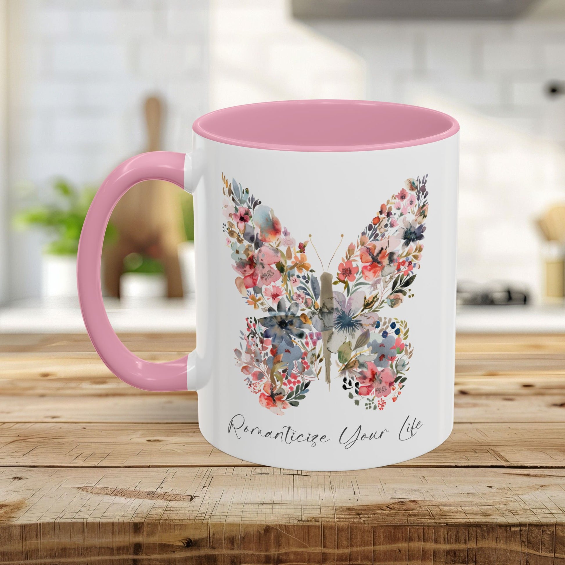 White ceramic mug with pink handle and interior, featuring a watercolor butterfly made of pink, blue, and green flowers.