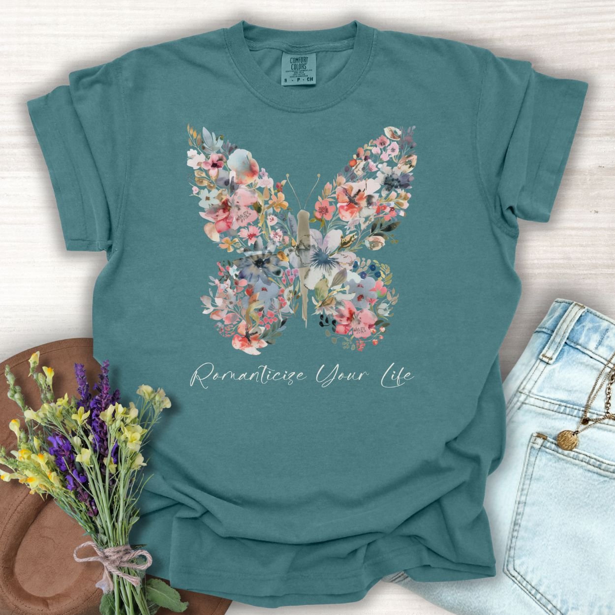 Blue Spruce garment-dyed cotton t-shirt with a floral butterfly design and "Romanticize Your Life" text.