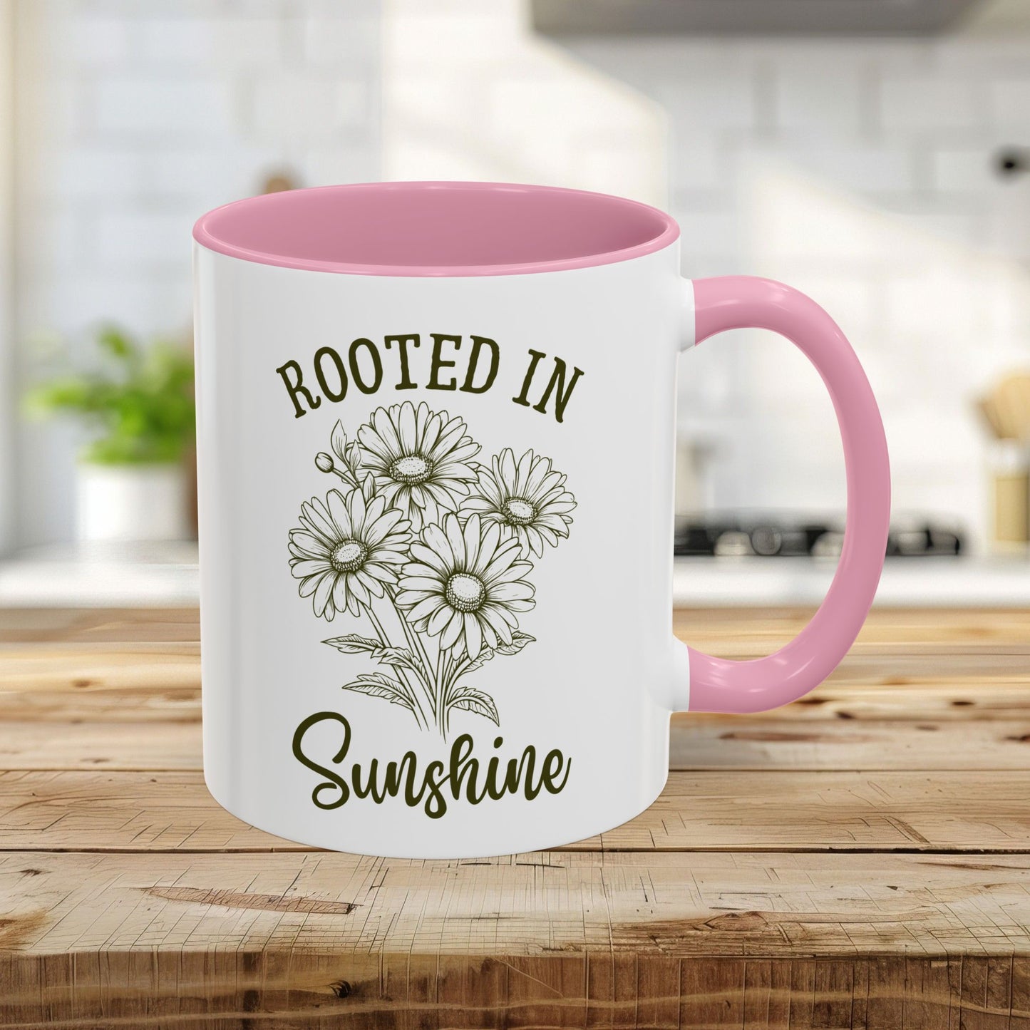 White ceramic 11oz mug with pink interior and handle, featuring hand-drawn daisies and "Rooted in Sunshine" text.