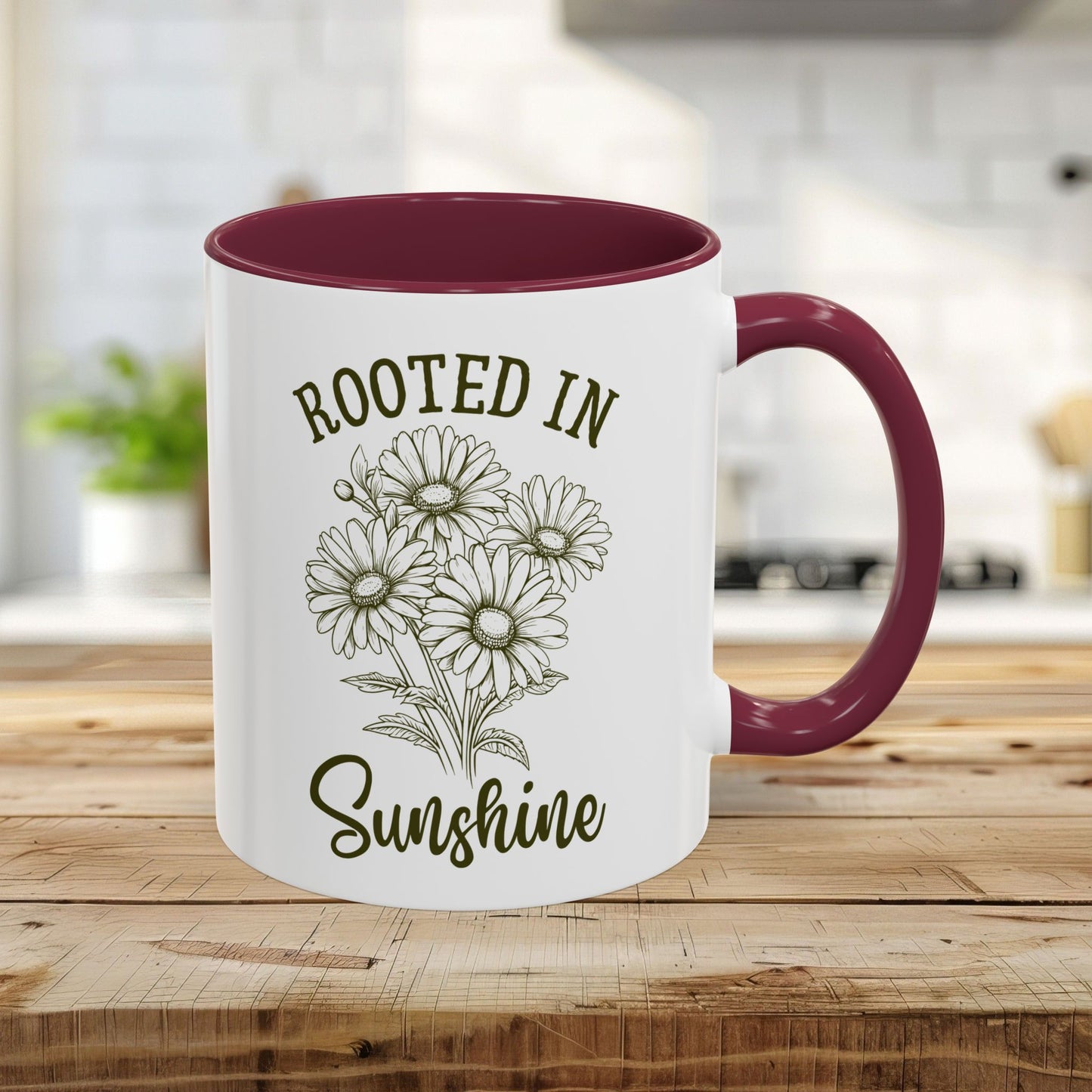 White ceramic mug with maroon interior and handle, featuring hand-drawn daisies and "Rooted in Sunshine" text.
