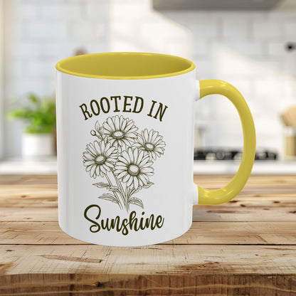 White 11oz ceramic mug with yellow interior/handle, "Rooted in Sunshine" text, and hand-drawn daisy print.