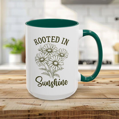 15oz white ceramic mug with green handle and interior, featuring hand-drawn daisies and "Rooted in Sunshine" text.