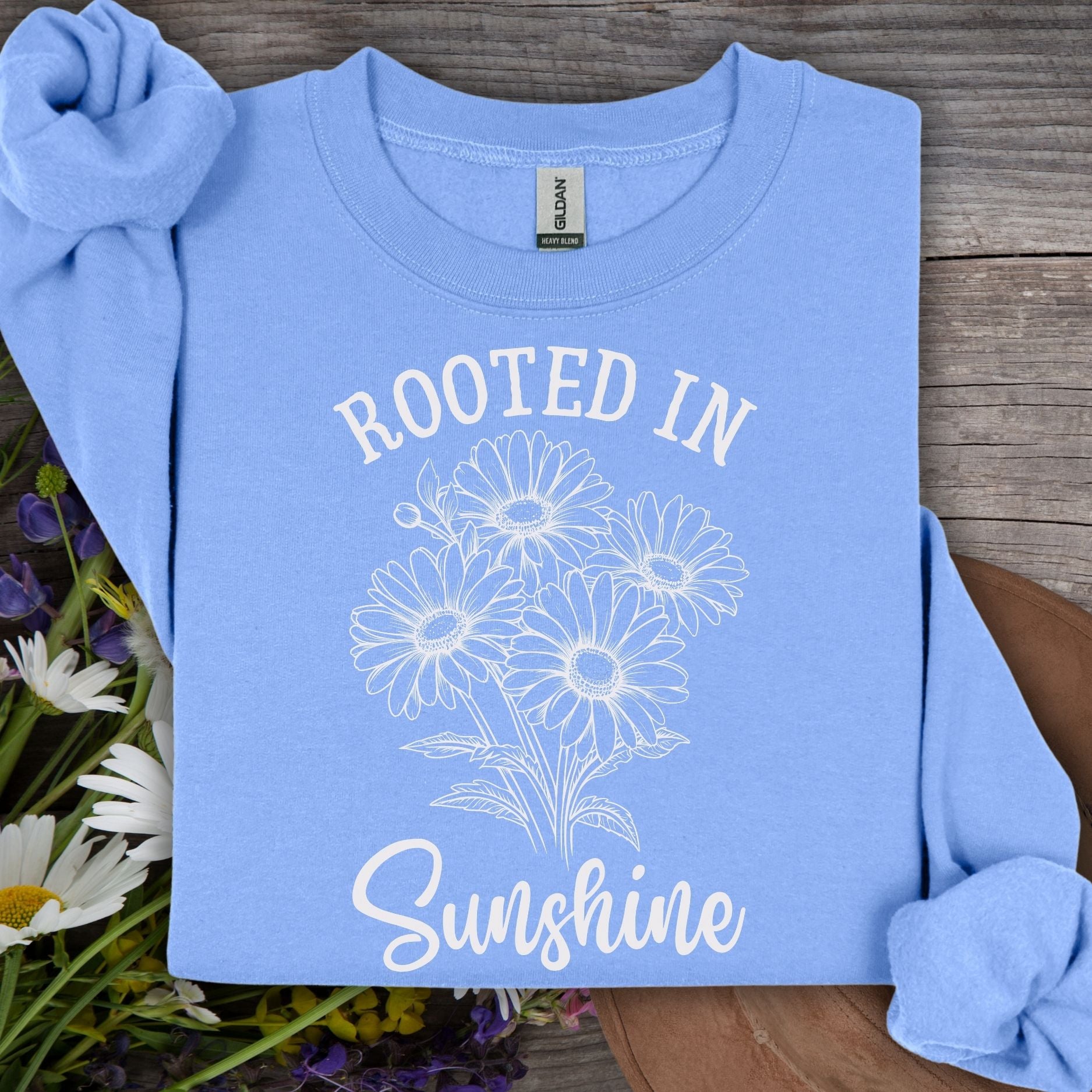Light blue unisex sweatshirt with white "Rooted in Sunshine" text and daisy bouquet graphic.