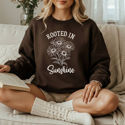 Woman wearing a brown "Rooted in Sunshine" daisy sweatshirt, sitting on a couch with a book.