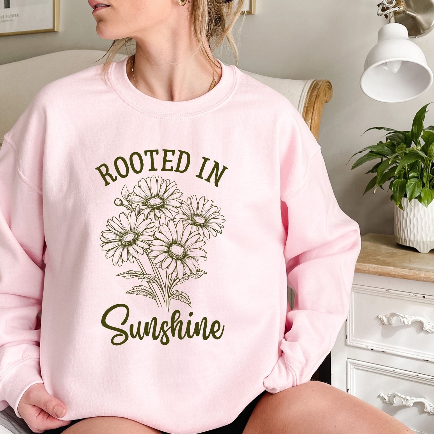 Pink unisex sweatshirt with "Rooted in Sunshine" text and a hand-drawn daisy bouquet design.