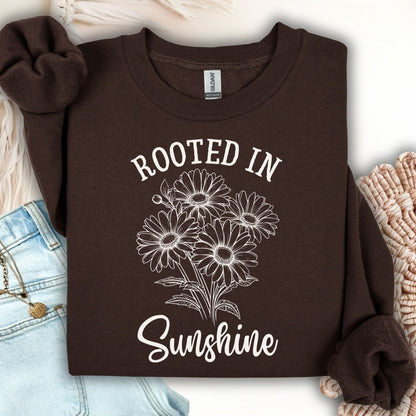 Dark chocolate unisex sweatshirt with "Rooted in Sunshine" and a daisy bouquet graphic.
