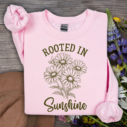 Light pink unisex sweatshirt with "Rooted in Sunshine" text and a hand-drawn daisy bouquet design.