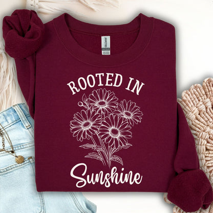 Maroon "Rooted in Sunshine" sweatshirt with white hand-drawn daisy bouquet, styled with jeans.
