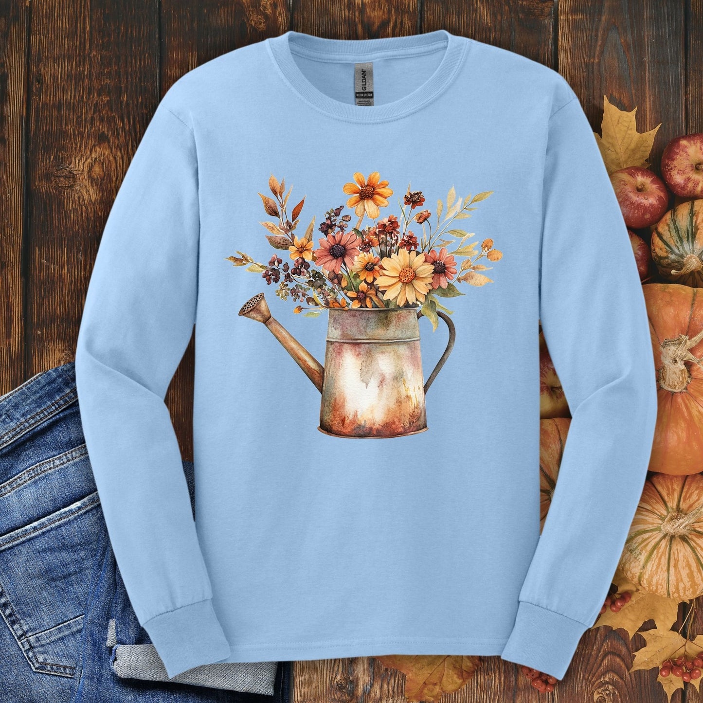 Light blue long sleeve tee with a vintage watercolor watering can overflowing with autumn wildflowers.