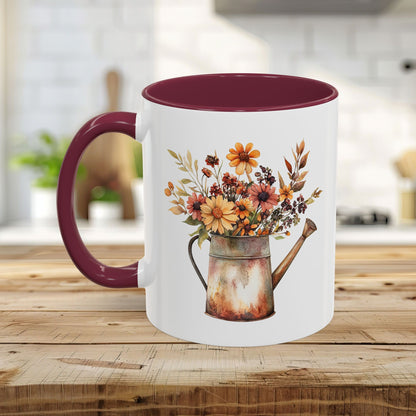 White ceramic mug with a rustic autumn floral watering can design, maroon interior, and C-shaped handle.