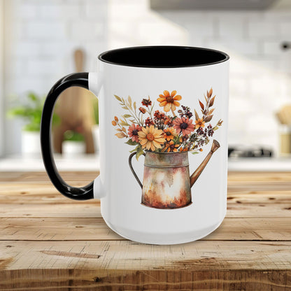 White ceramic mug with black interior and handle, featuring a rustic watercolor watering can filled with autumn florals.