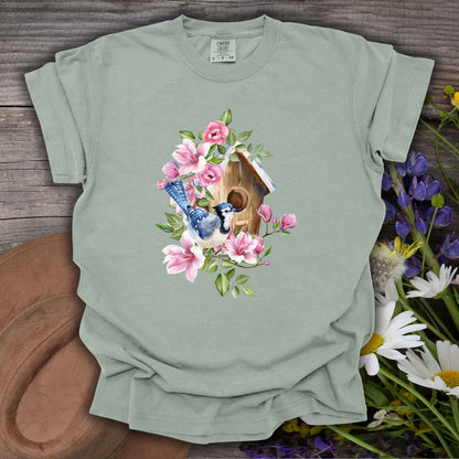 Bay S Comfort Colors t-shirt with a watercolor blue jay, birdhouse, and pink magnolia illustration.