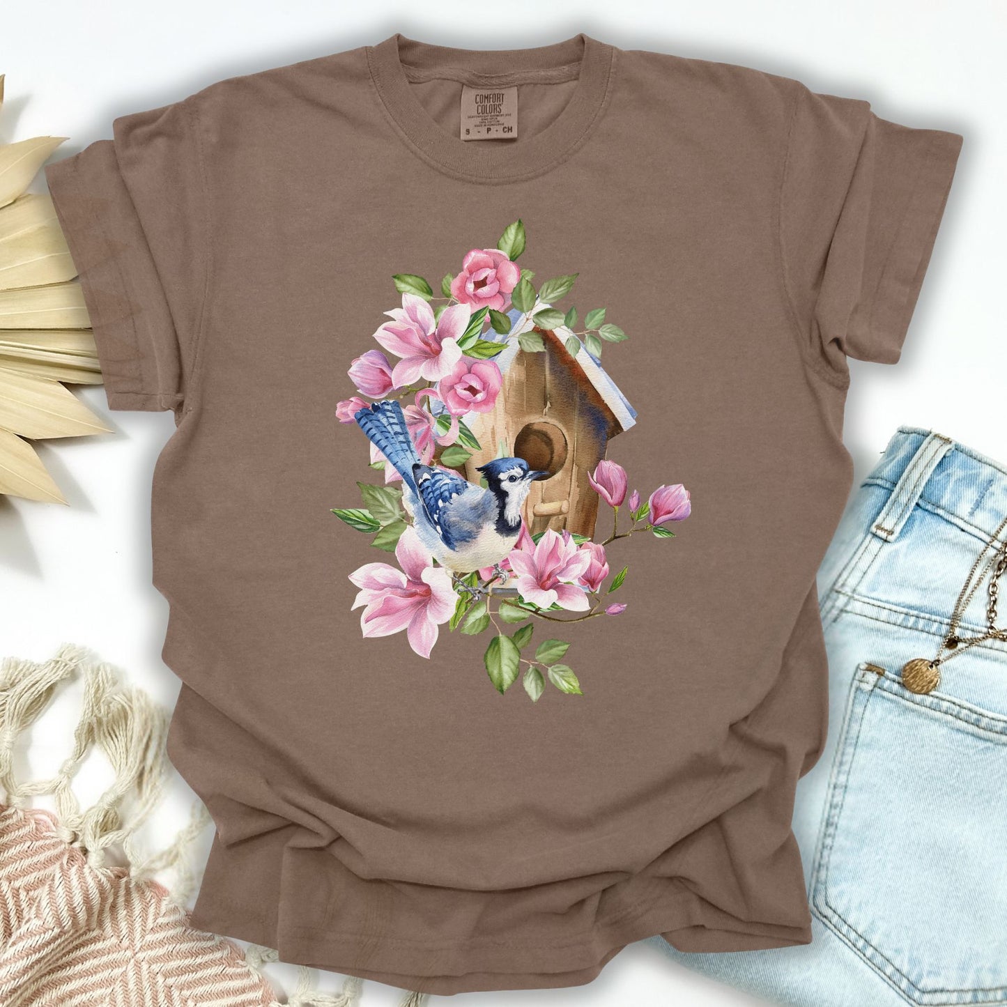 Espresso S t-shirt with a watercolor blue jay on a rustic birdhouse surrounded by pink flowers.