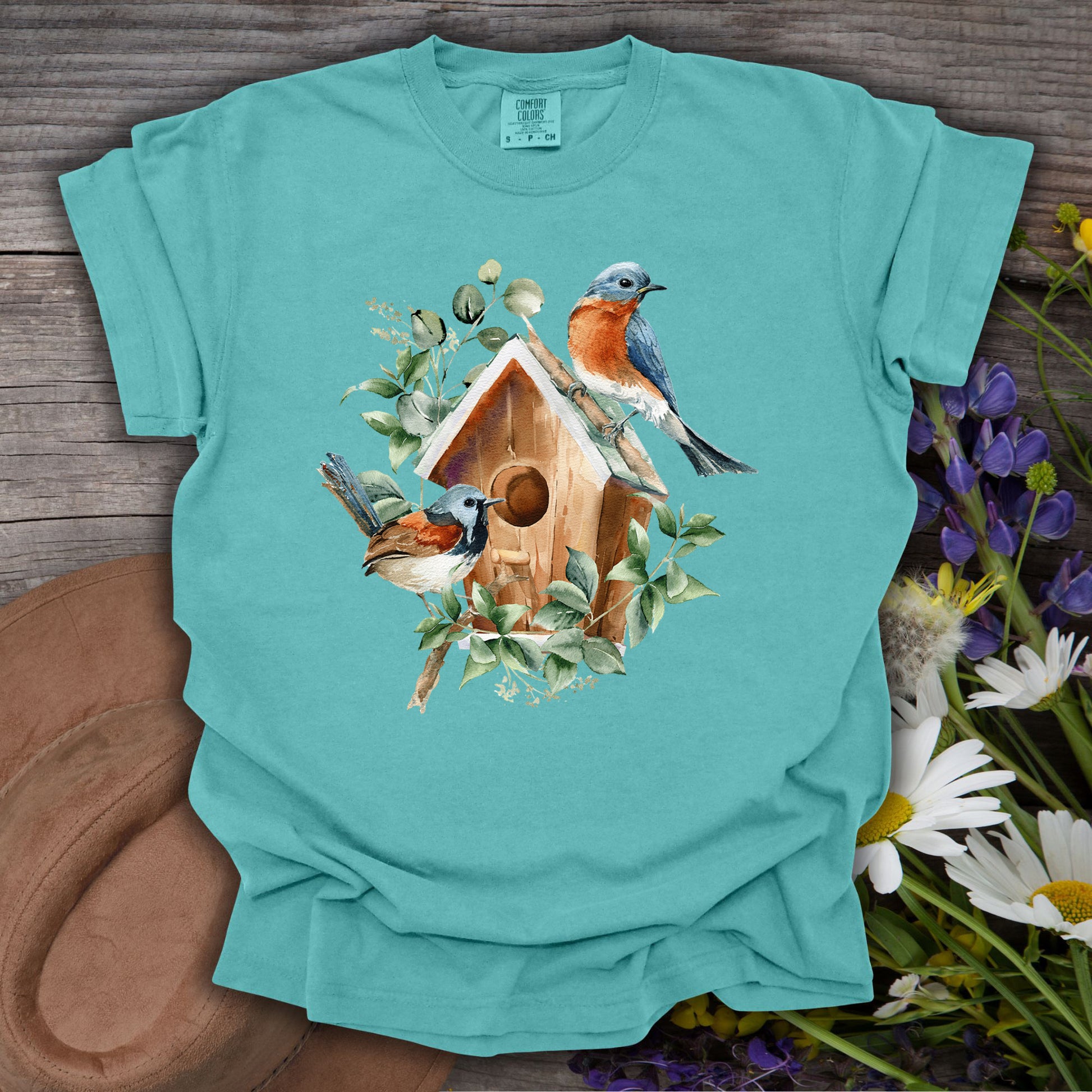 Watercolor rustic birdhouse with two bluebirds and foliage on a relaxed-fit, garment-dyed teal t-shirt.