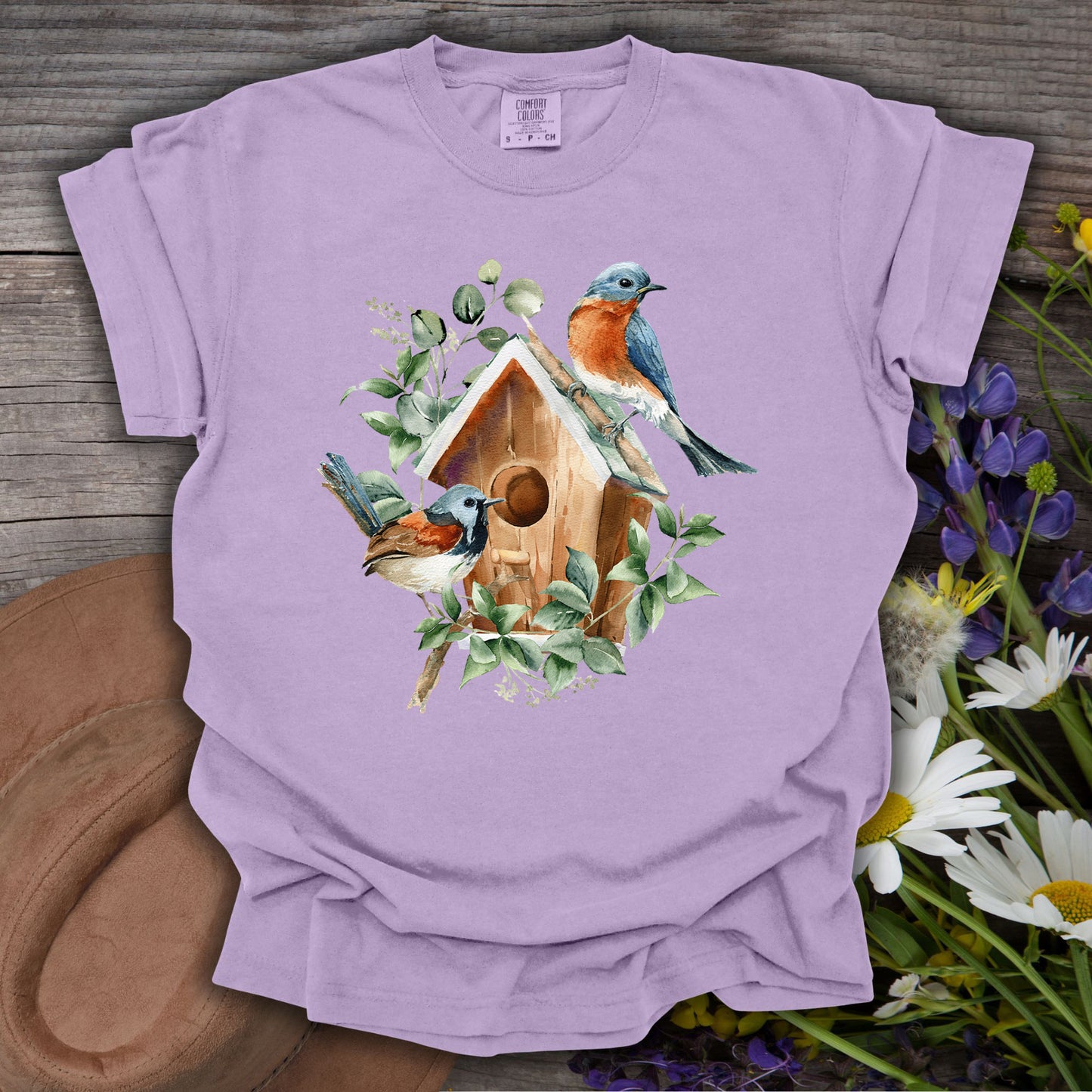 Watercolor rustic birdhouse with two bluebirds and eucalyptus on a relaxed-fit, garment-dyed lavender t-shirt.