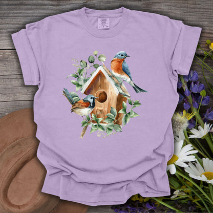 Watercolor rustic birdhouse with two bluebirds and eucalyptus on a relaxed-fit, garment-dyed lavender t-shirt.