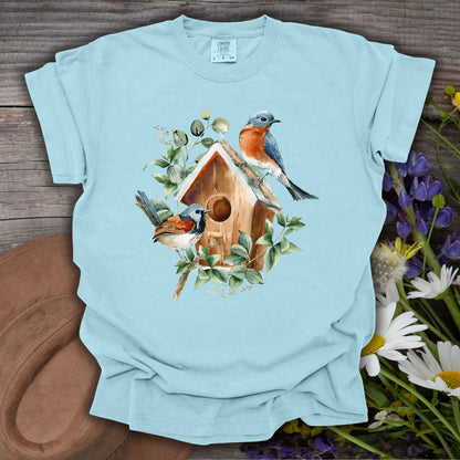 Chambray blue t-shirt with a watercolor rustic birdhouse and two bluebirds surrounded by foliage.