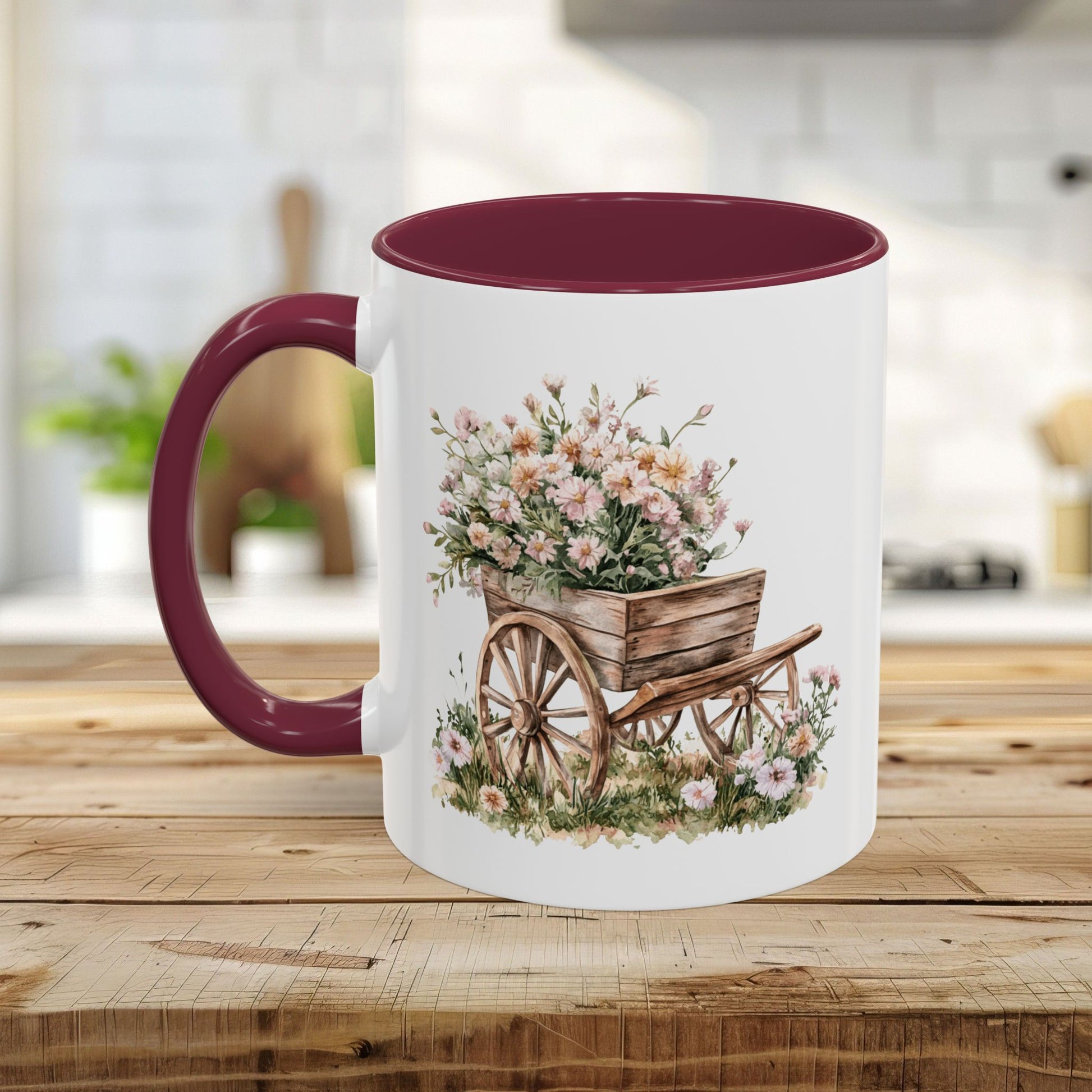 White ceramic mug with a maroon handle and interior, featuring a watercolor wheelbarrow overflowing with pink flowers.