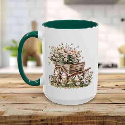White ceramic mug with green handle and interior, featuring a watercolor wheelbarrow overflowing with pink flowers.