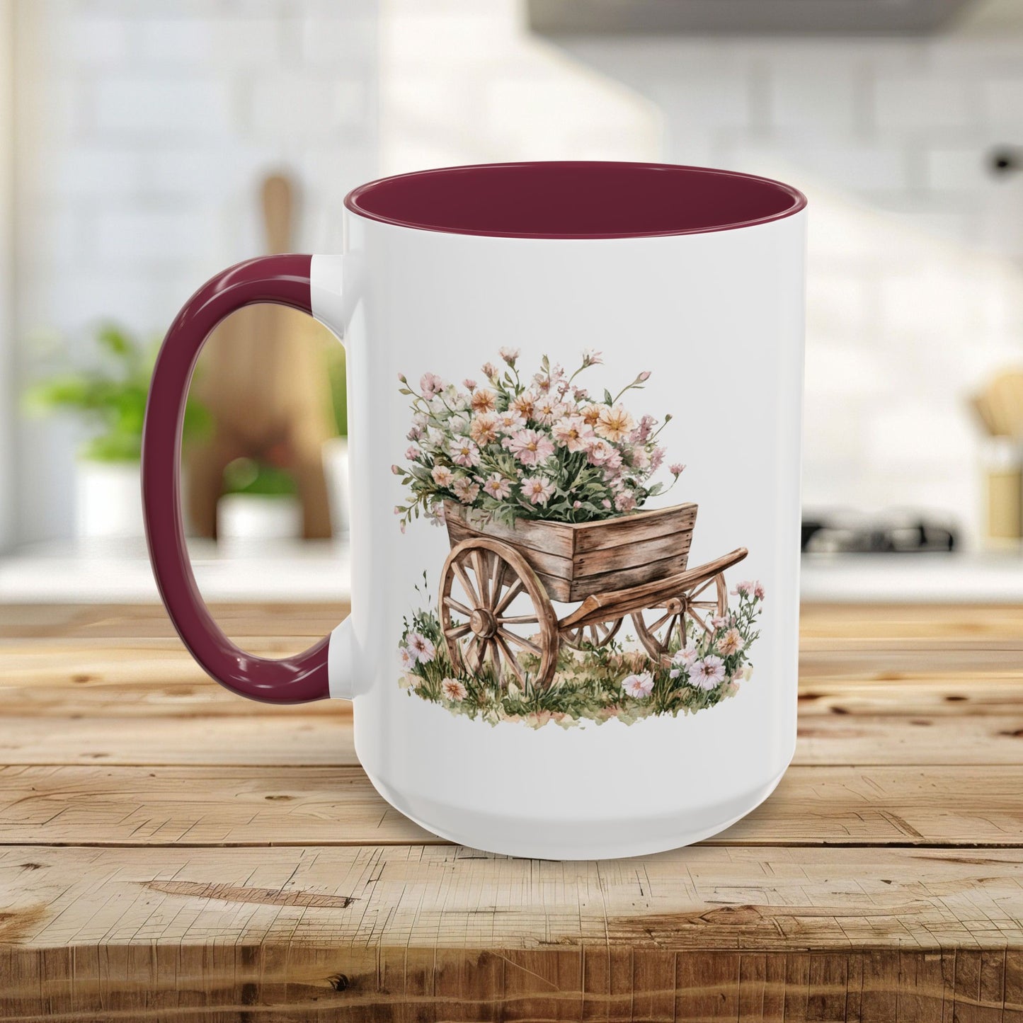 White ceramic mug with a maroon handle and interior, featuring a watercolor wheelbarrow overflowing with pink blooms.