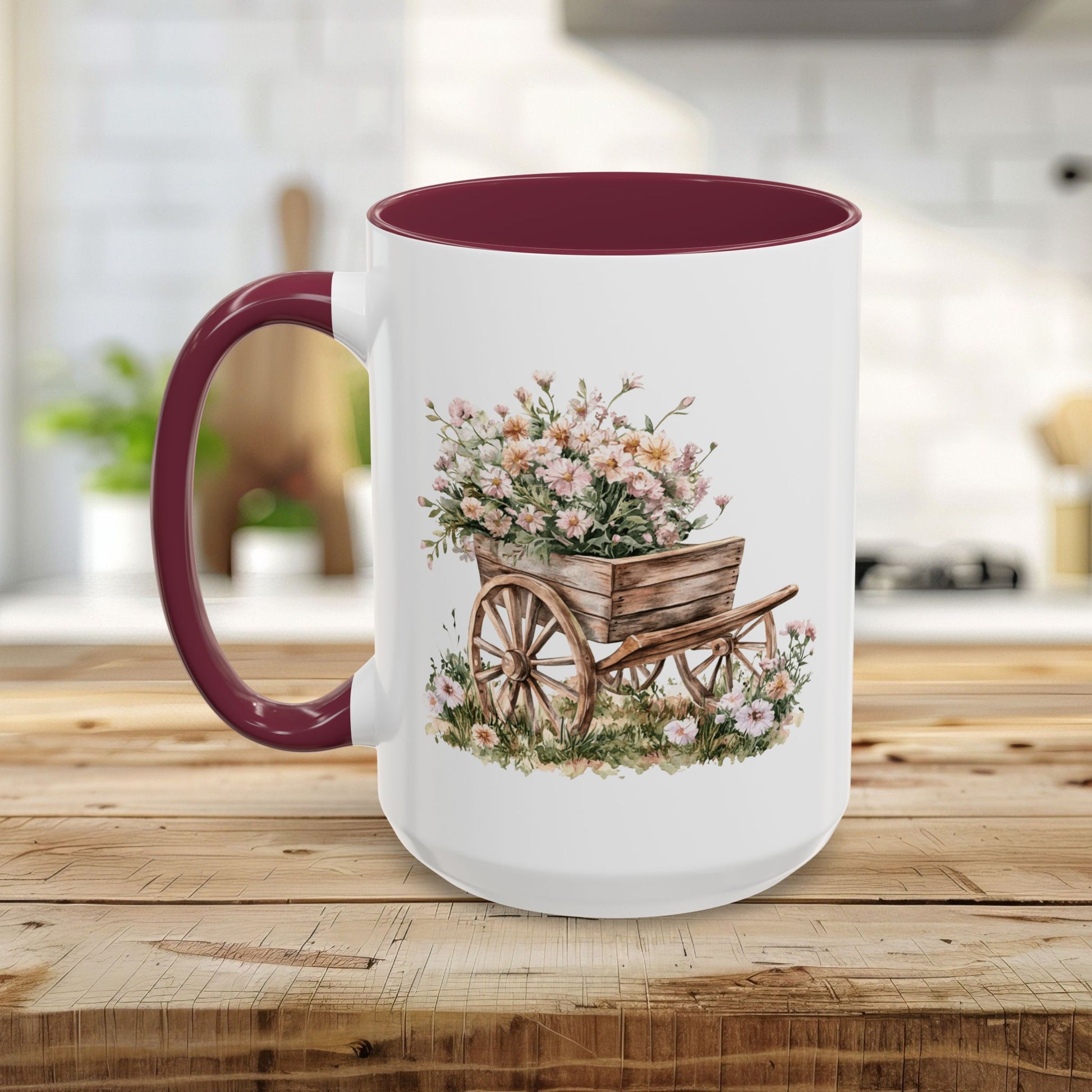 White ceramic mug with a maroon handle and interior, featuring a watercolor wheelbarrow overflowing with pink blooms.