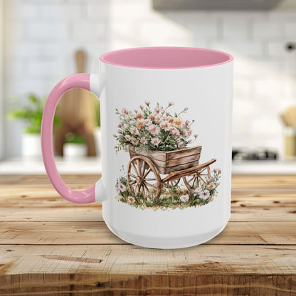 White ceramic mug with pink interior and handle, featuring a watercolor wheelbarrow overflowing with pink blooms.