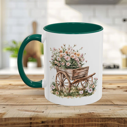 White ceramic mug with green interior and handle, featuring a watercolor wheelbarrow overflowing with pink blooms.
