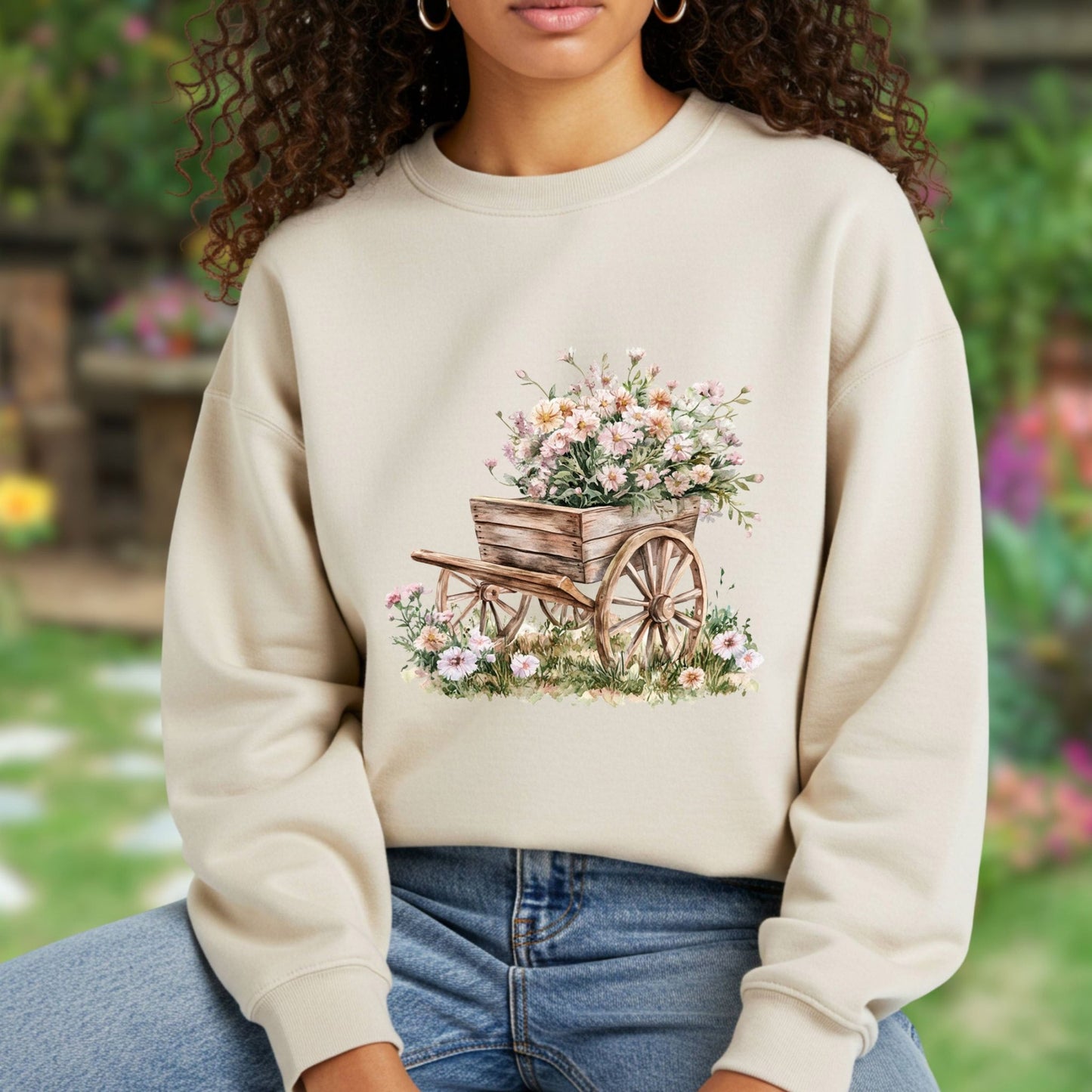 Beige sweatshirt with a watercolor illustration of a rustic wooden wagon overflowing with pink carnations.