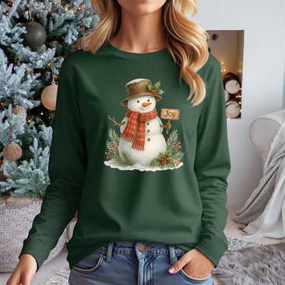 Dark green long-sleeve tee with a watercolor snowman holding a "Joy" sign, holly, and snowy branches.